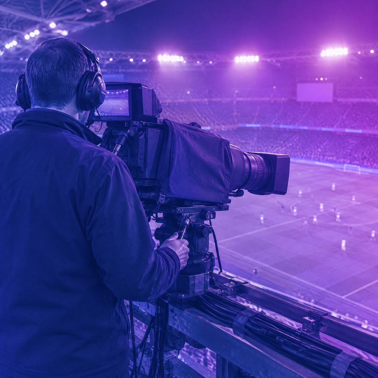 A broadcast camera operator seen from behind on a stadium gantry, the camera aimed at the floodlit pitch below, graded in TAG Blue and purple, with a gold circle drawn around the camera lens.